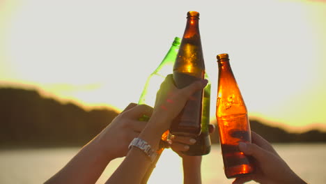 People-are-dancing-with-hands-up-and-clink-beer-from-glass-bottles.-This-is-crazy-party-at-sunset-on-the-lake-coast.